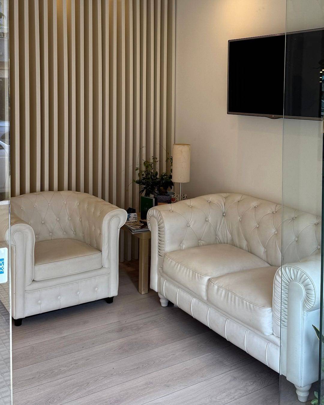 La sala de espera, con sofá y sillón blancos capitoné